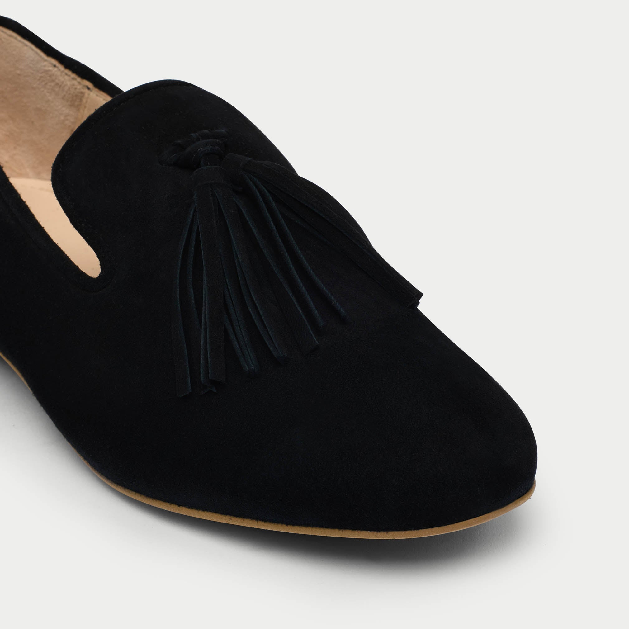 Black suede loafer with tassel on a light gray background