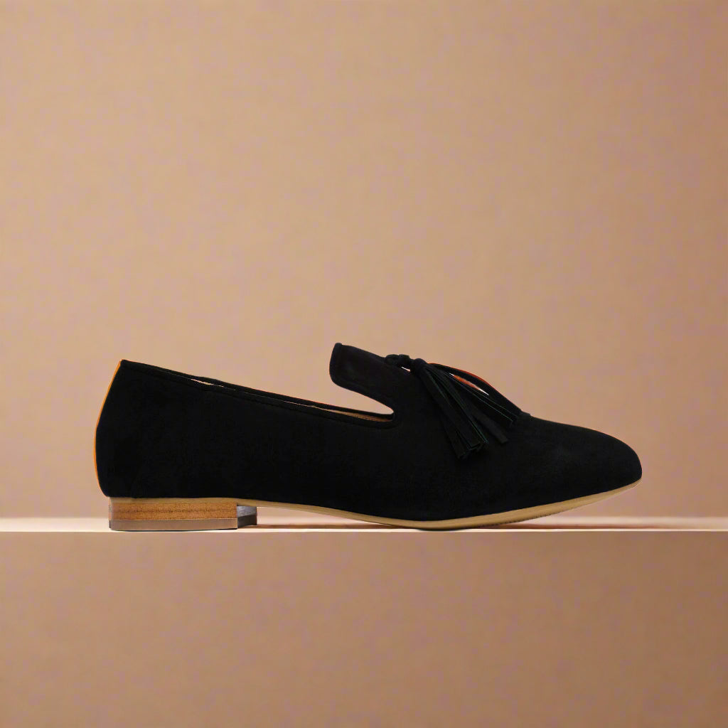 Black suede loafer shoe on a light orange background