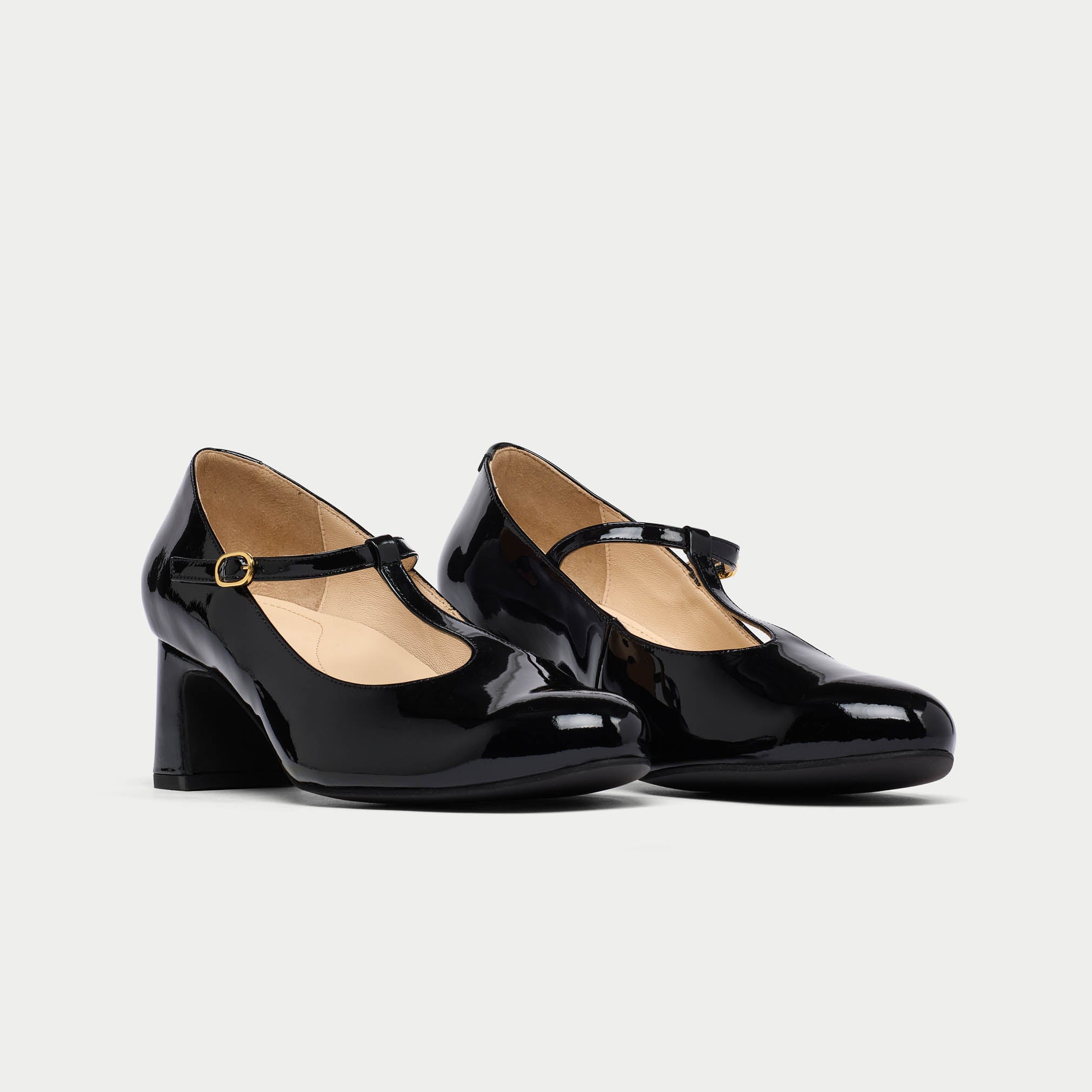 Pair of black patent leather shoes with a strap on a light gray background