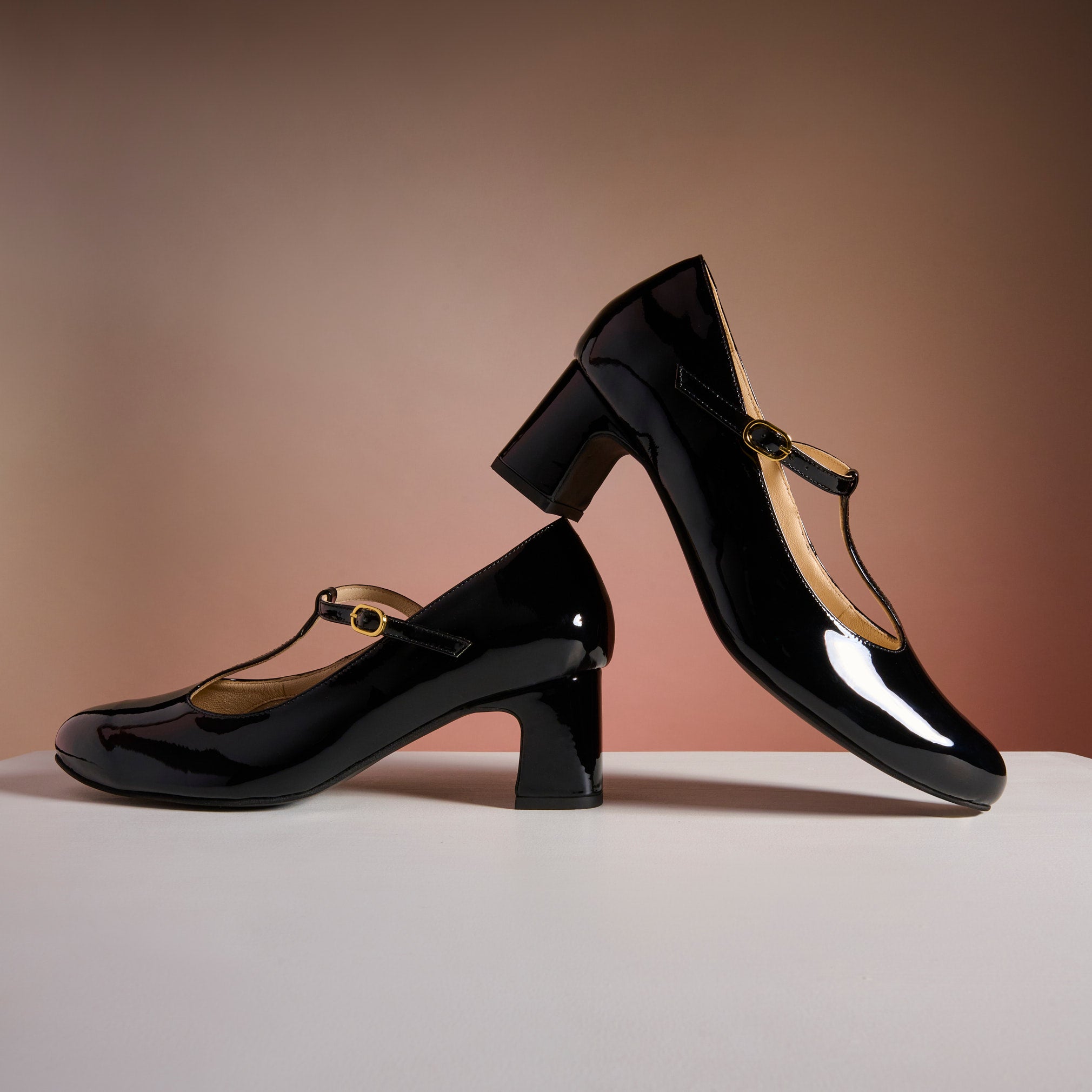 Pair of black patent leather shoes with gold straps on a neutral background