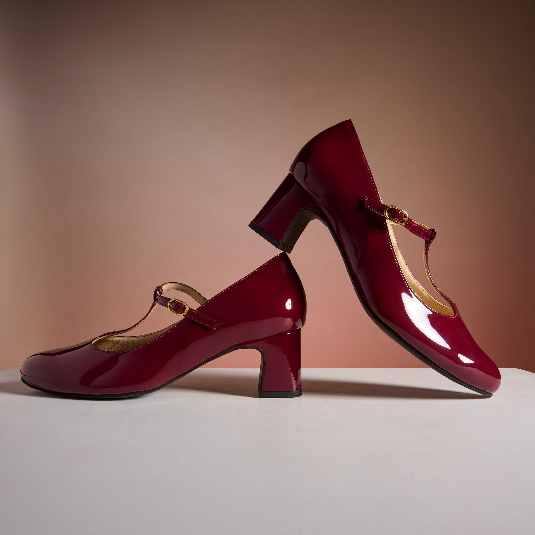 Pair of red high-heeled shoes with a strap on a neutral background