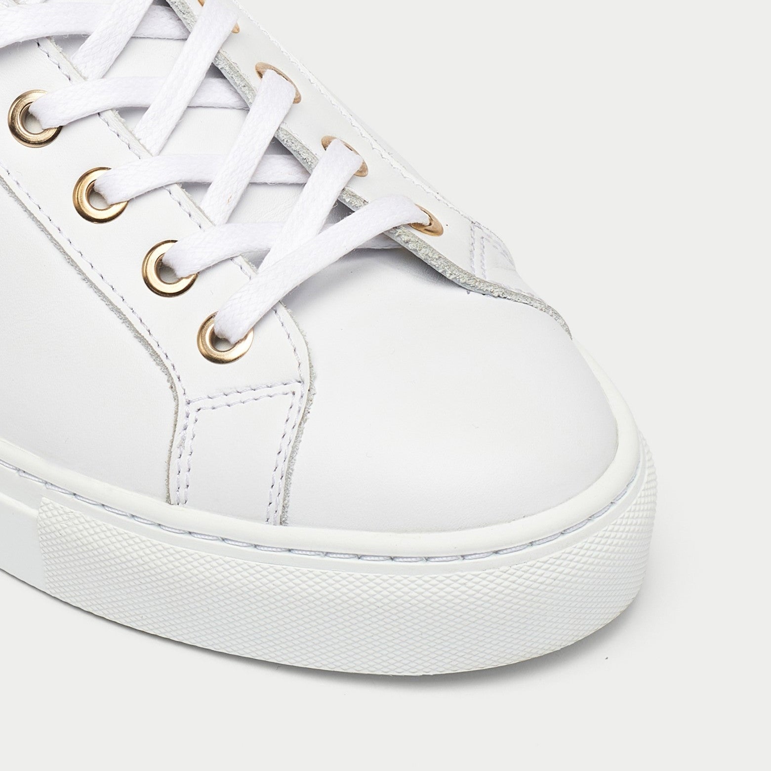 White sneaker with gold eyelets on a light gray background