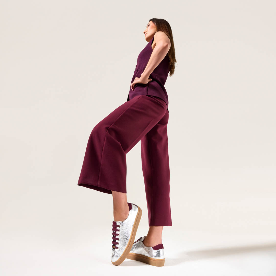 Woman wearing a purple jumpsuit with silver star sneakers on a plain background