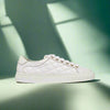 A white quilted sneaker with lace-up closure, displayed against a geometric shadowed background.