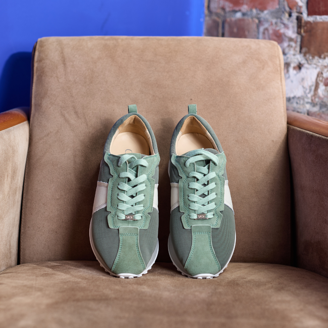 Pair of green sneakers on a brown couch with a blue wall and brick wall in the background.