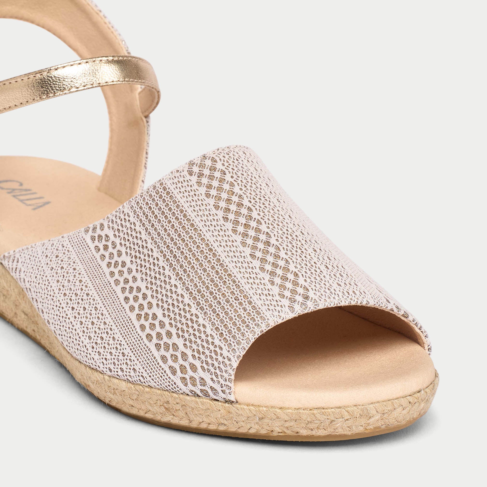 Gold sandal with textured strap on a light gray background