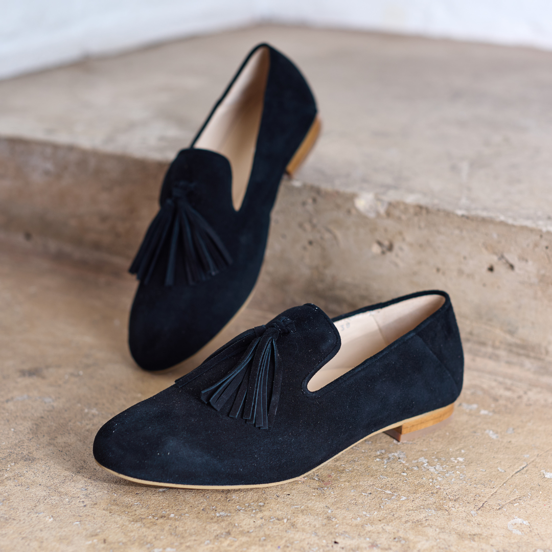 Pair of black suede loafers with tassels on a textured surface