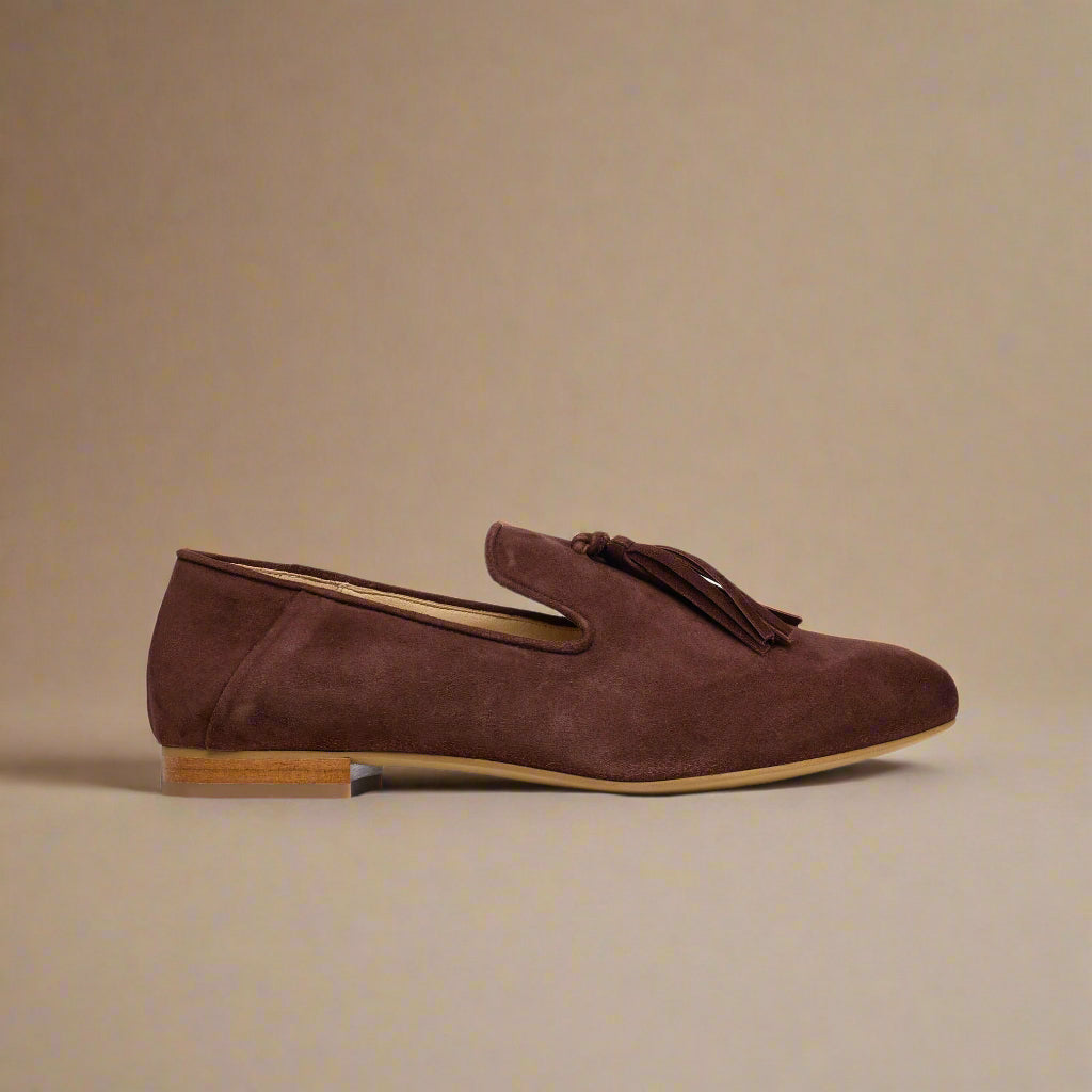 Brown suede loafer with tassel on a light beige background