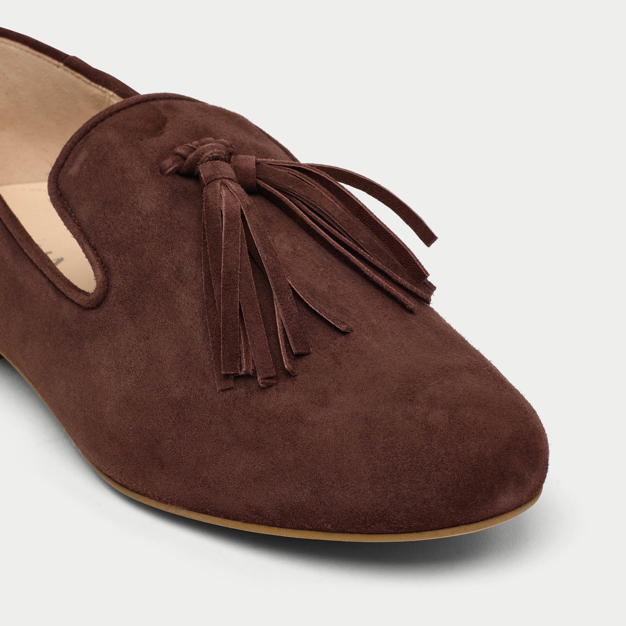 Brown suede loafer with tassel on a light gray background