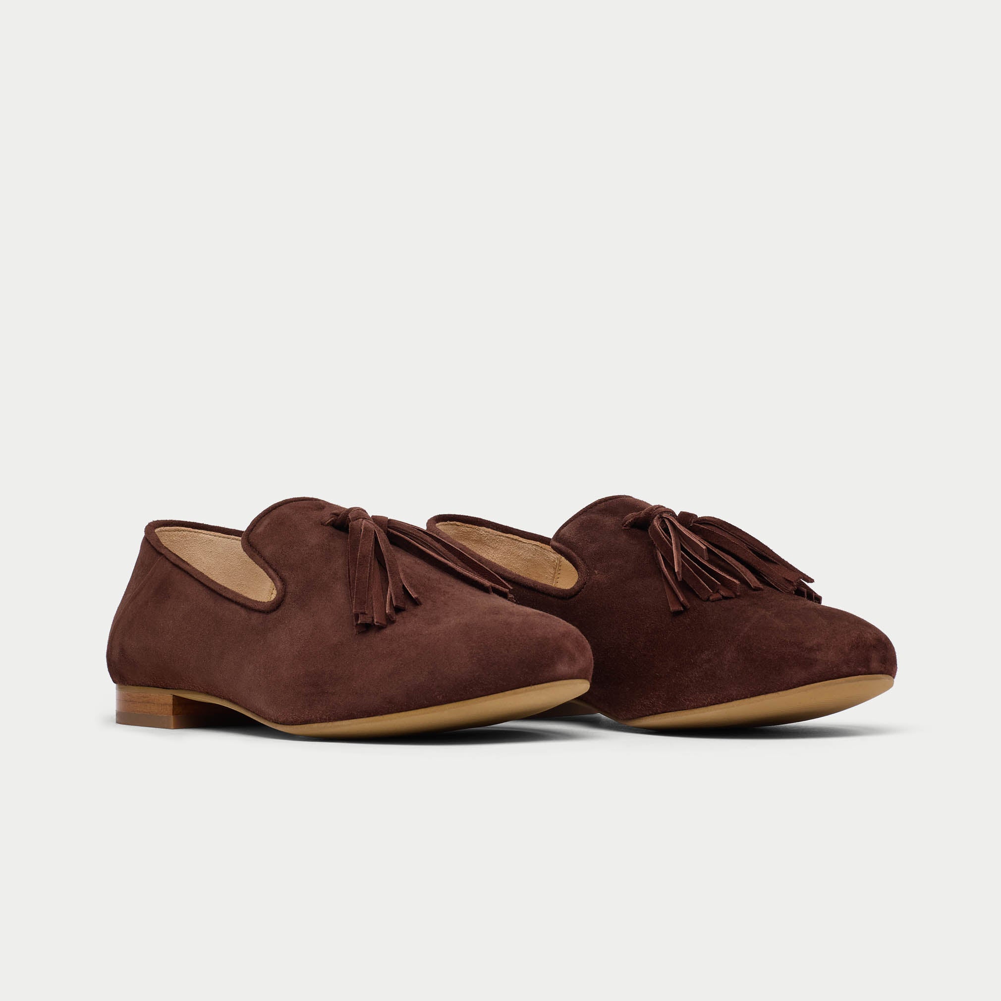Pair of brown suede shoes with tassels on a light gray background