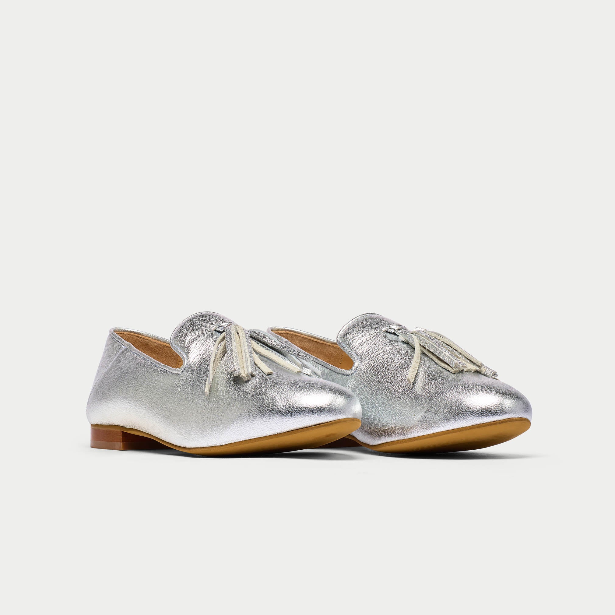 Pair of silver loafers with tassels on a light gray background