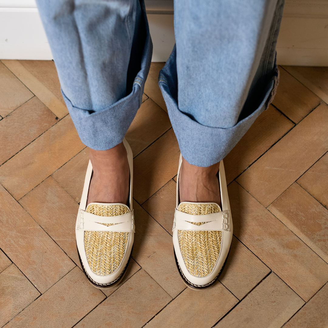 Person wearing white loafers with straw texture on a wooden floor