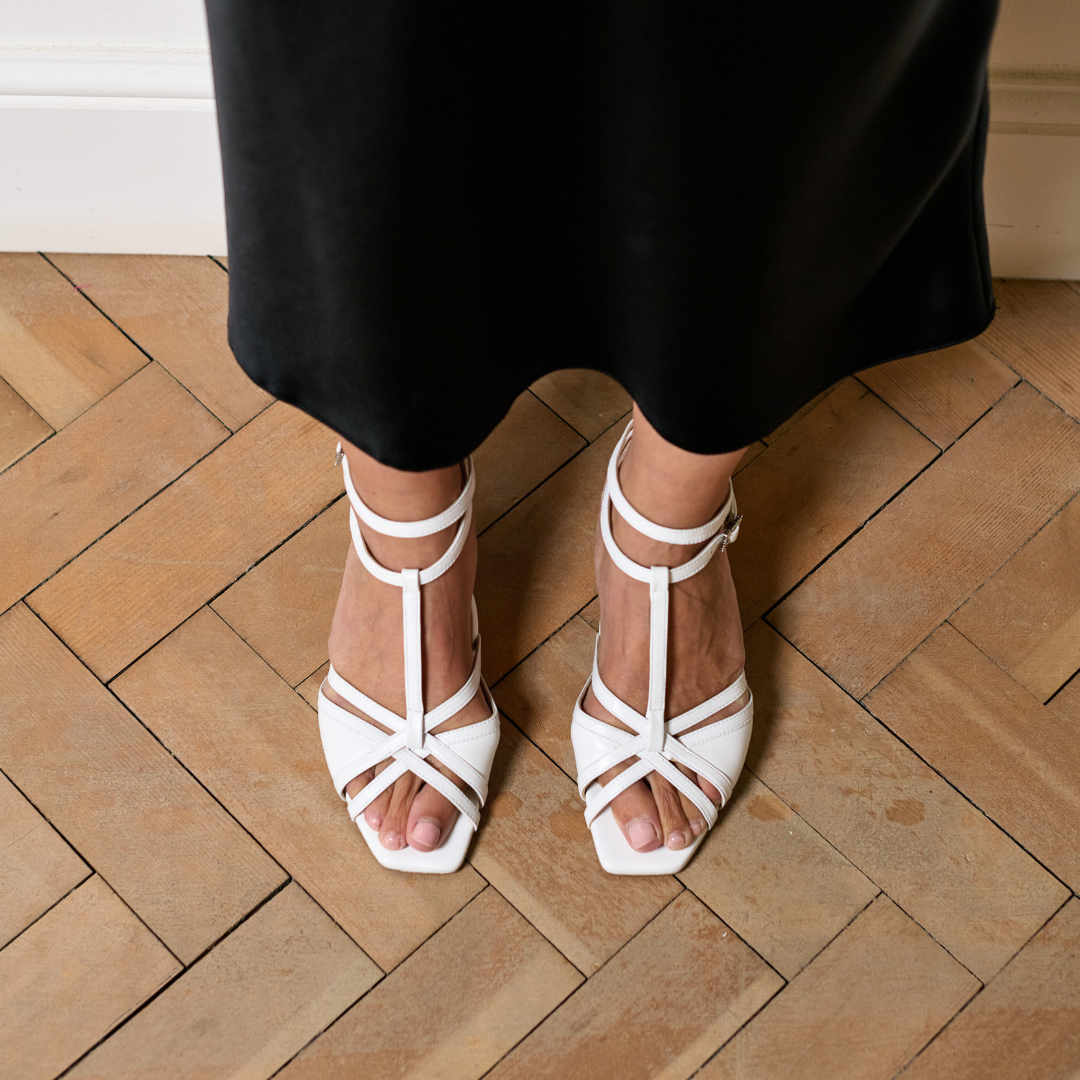 White strappy sandals worn on a wooden floor