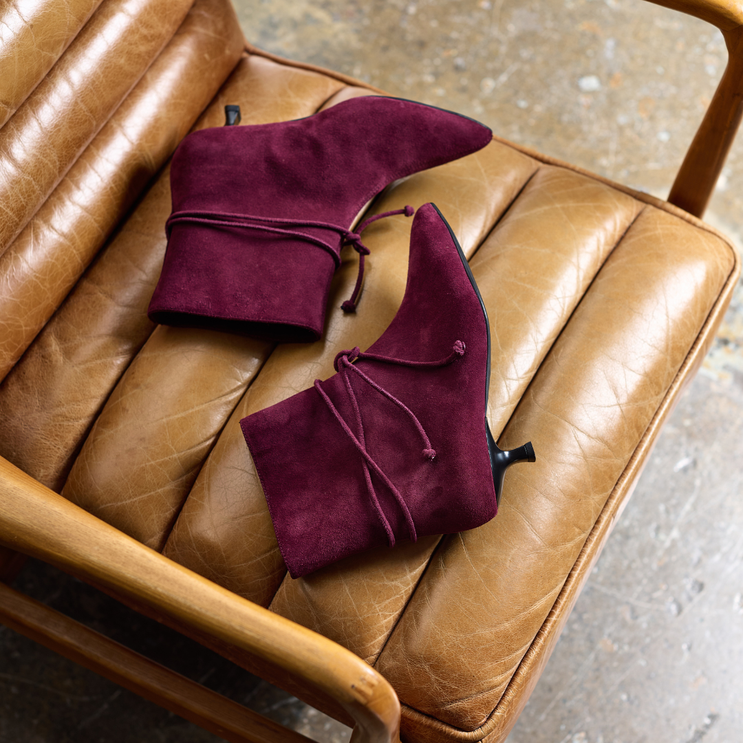 Pair of maroon suede shoes on a brown leather chair.
