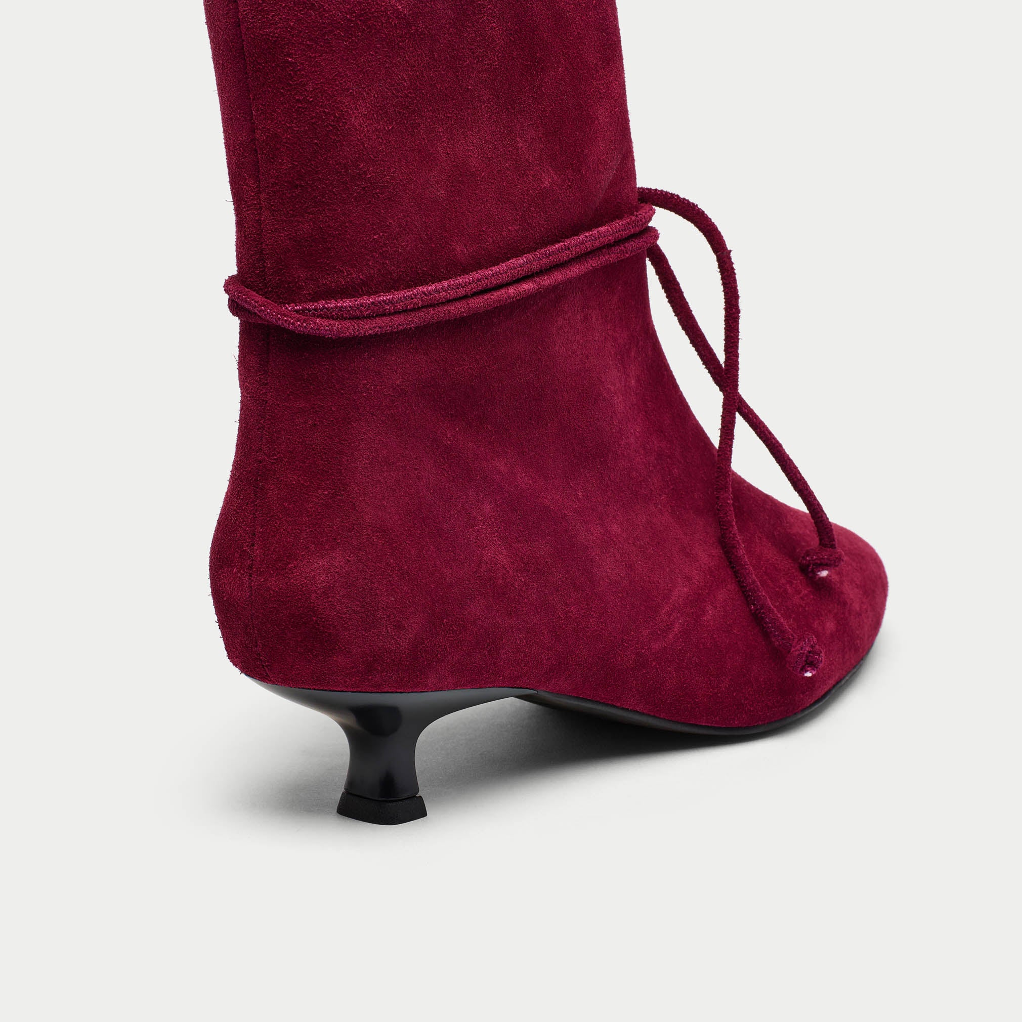 Maroon suede boot with a tie detail on a light gray background