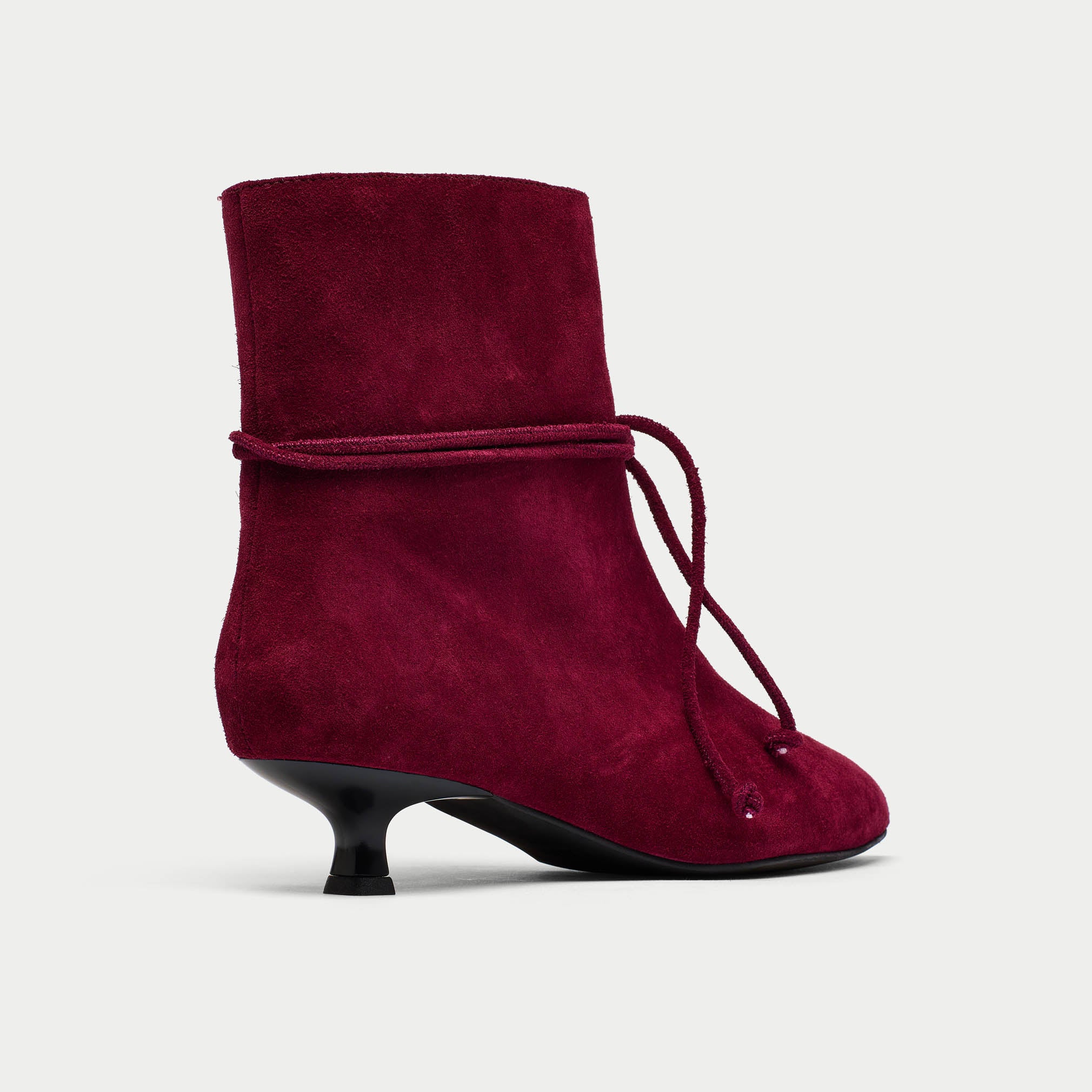 Maroon suede ankle boot with a black heel on a light gray background