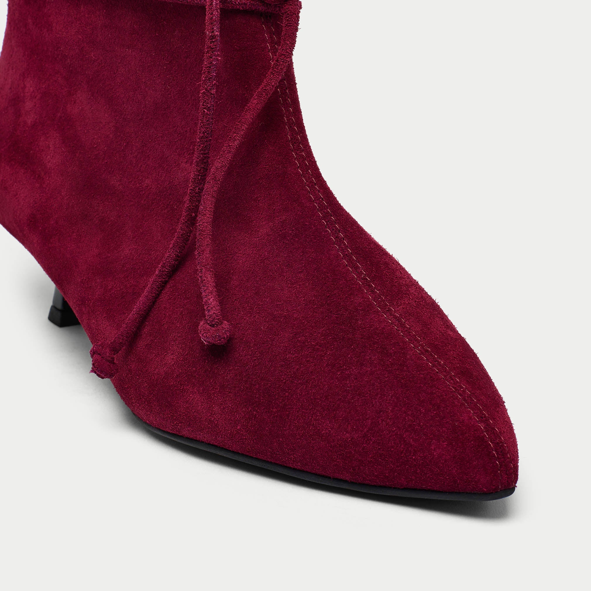 Maroon suede boot with a pointed toe on a light gray background