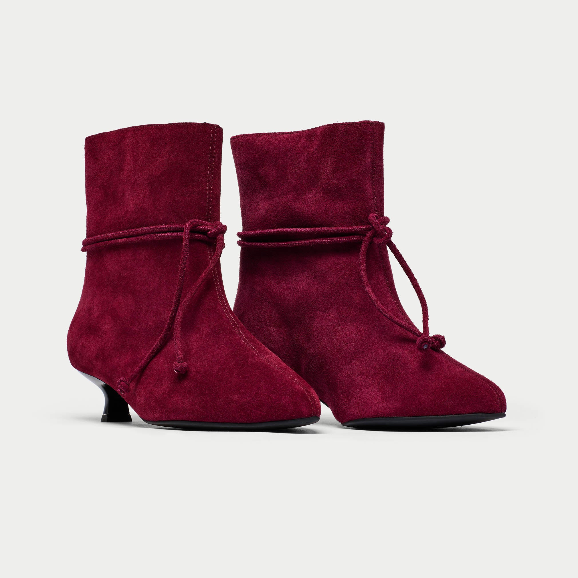 Pair of maroon ankle boots with tied design on a light gray background