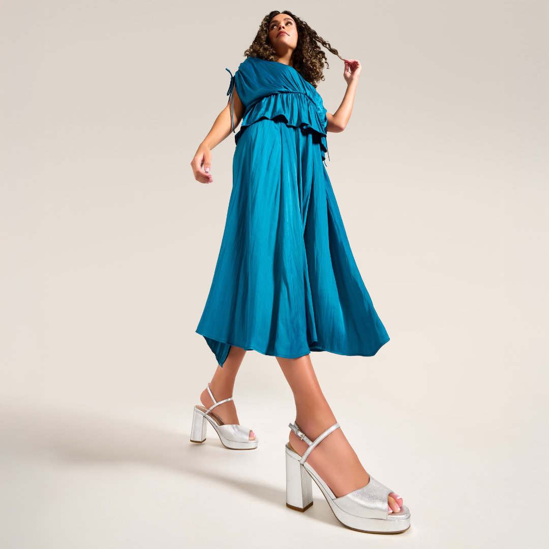 Woman wearing a blue dress and silver high-heeled shoes on a beige background