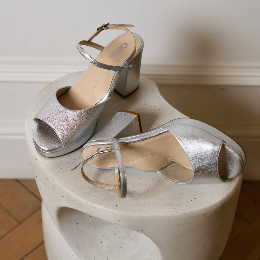 Pair of silver high-heeled shoes on a textured white surface.