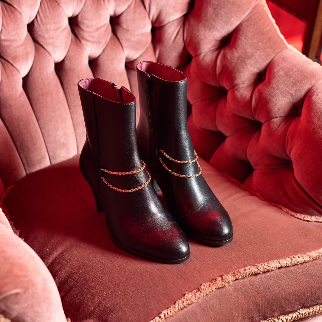 Black Maya ankle boots with gold accents on a red plush chair