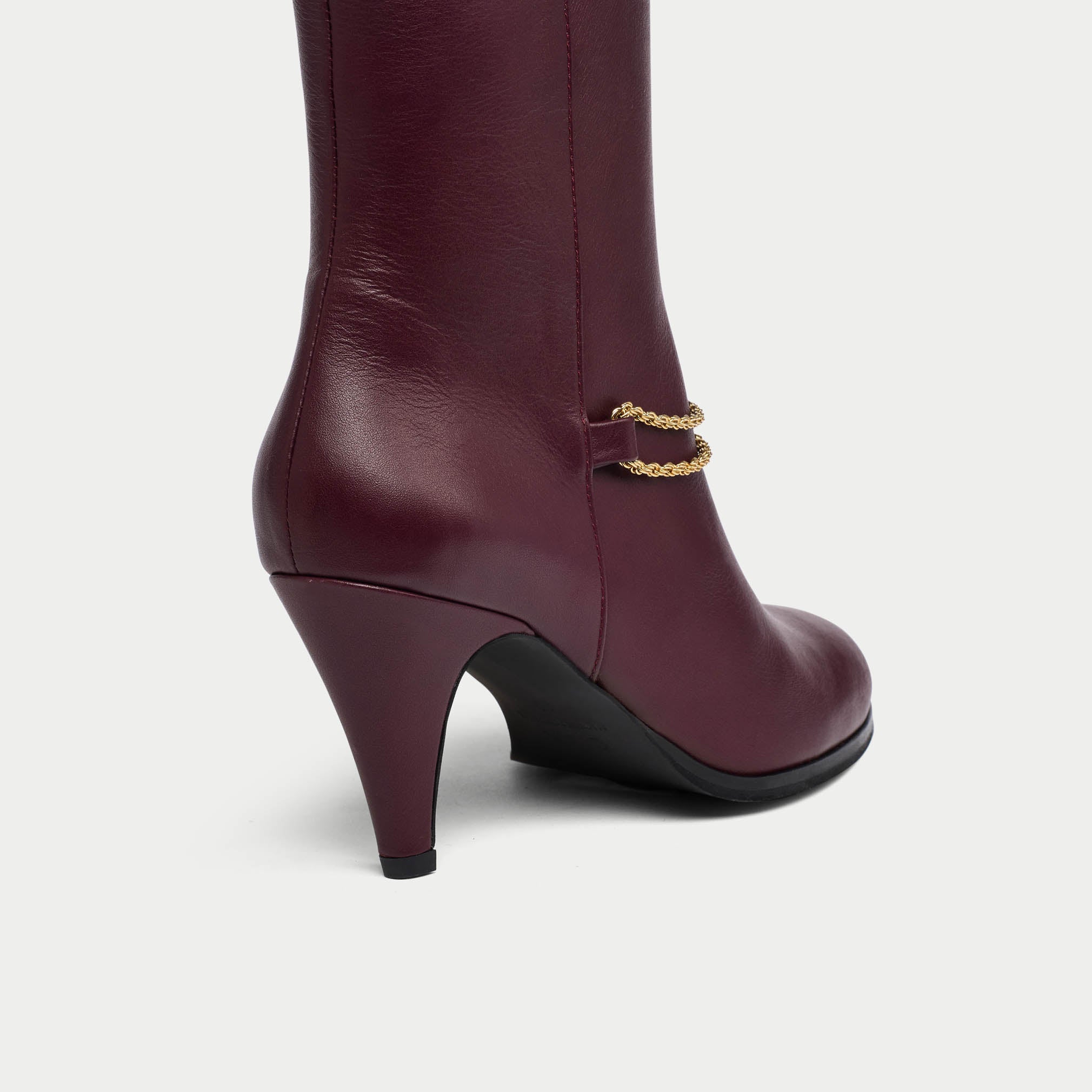 Maya cherry leather boot with gold chain detail on a white background heel close-up