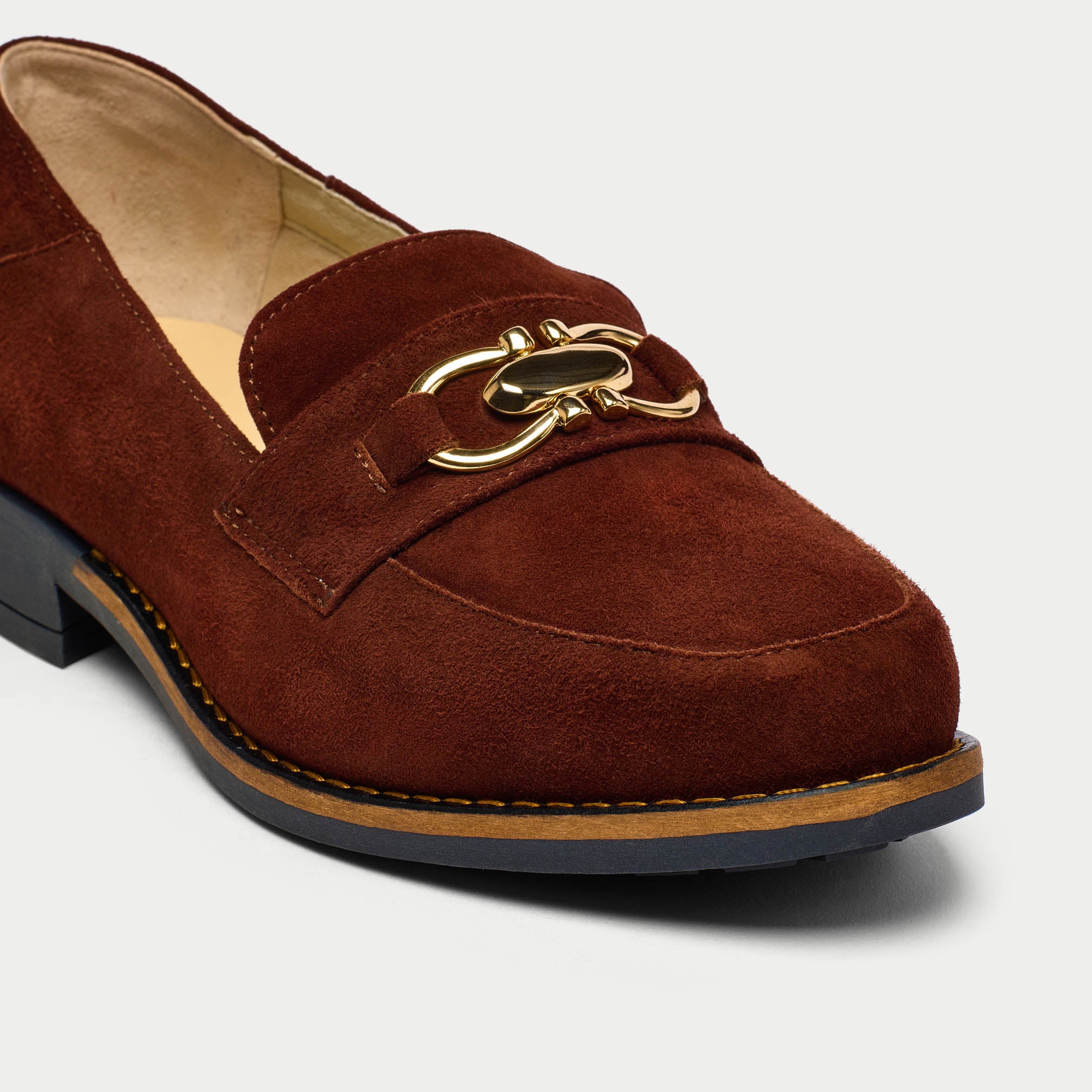 Brown suede loafer with gold chain detail on a light gray background