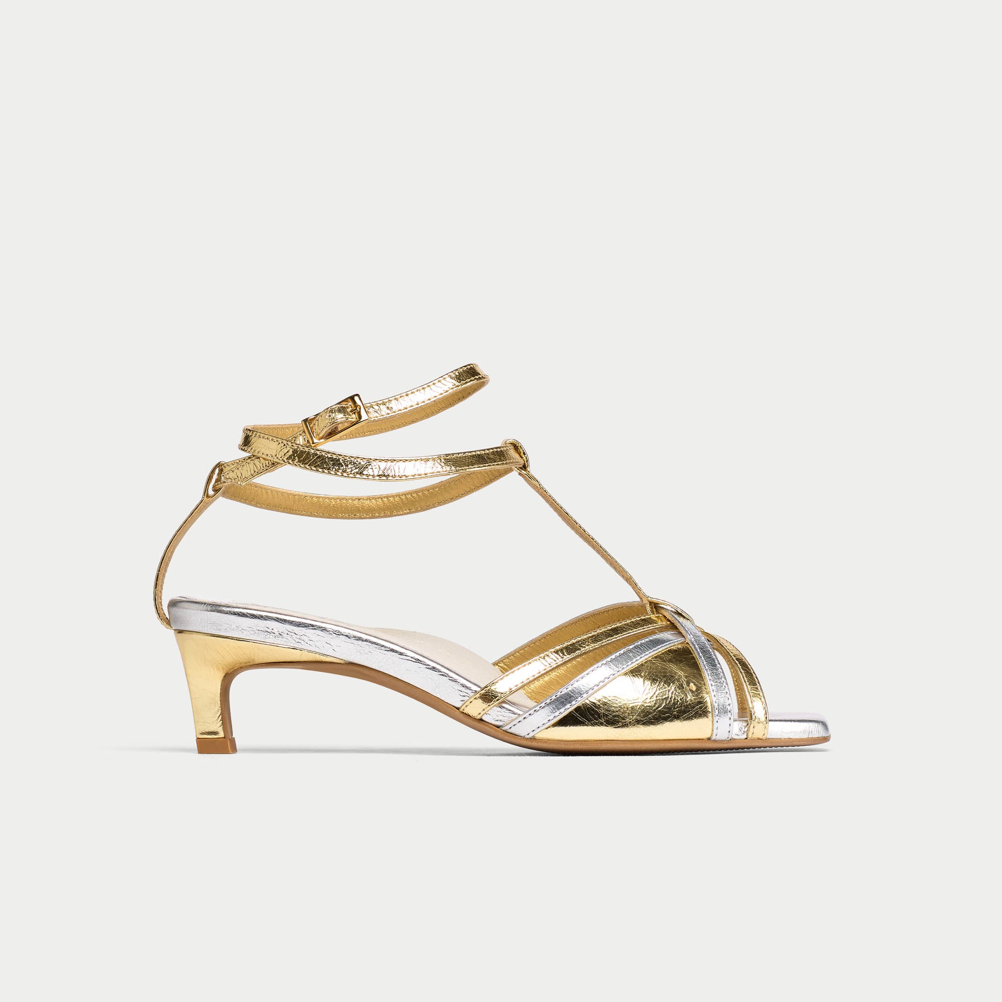 Gold sandal with clear straps on a light gray background