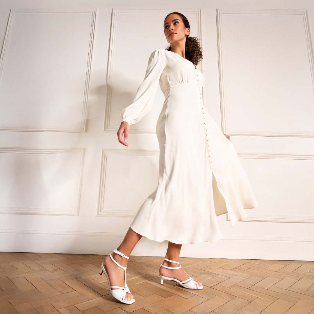Woman in a white dress standing against a white paneled wall.