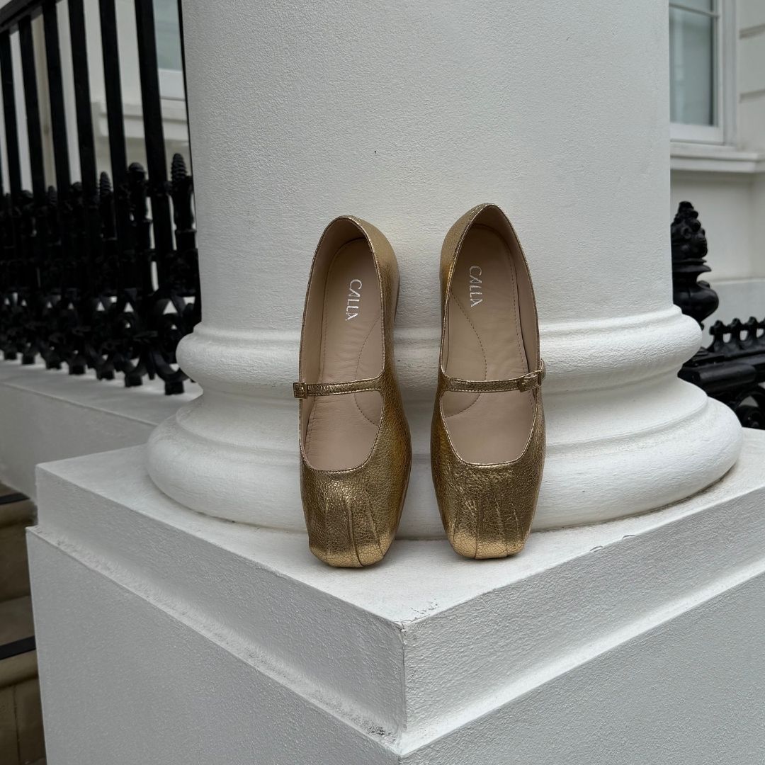 Gold shoes on a white pedestal with a black railing in the background