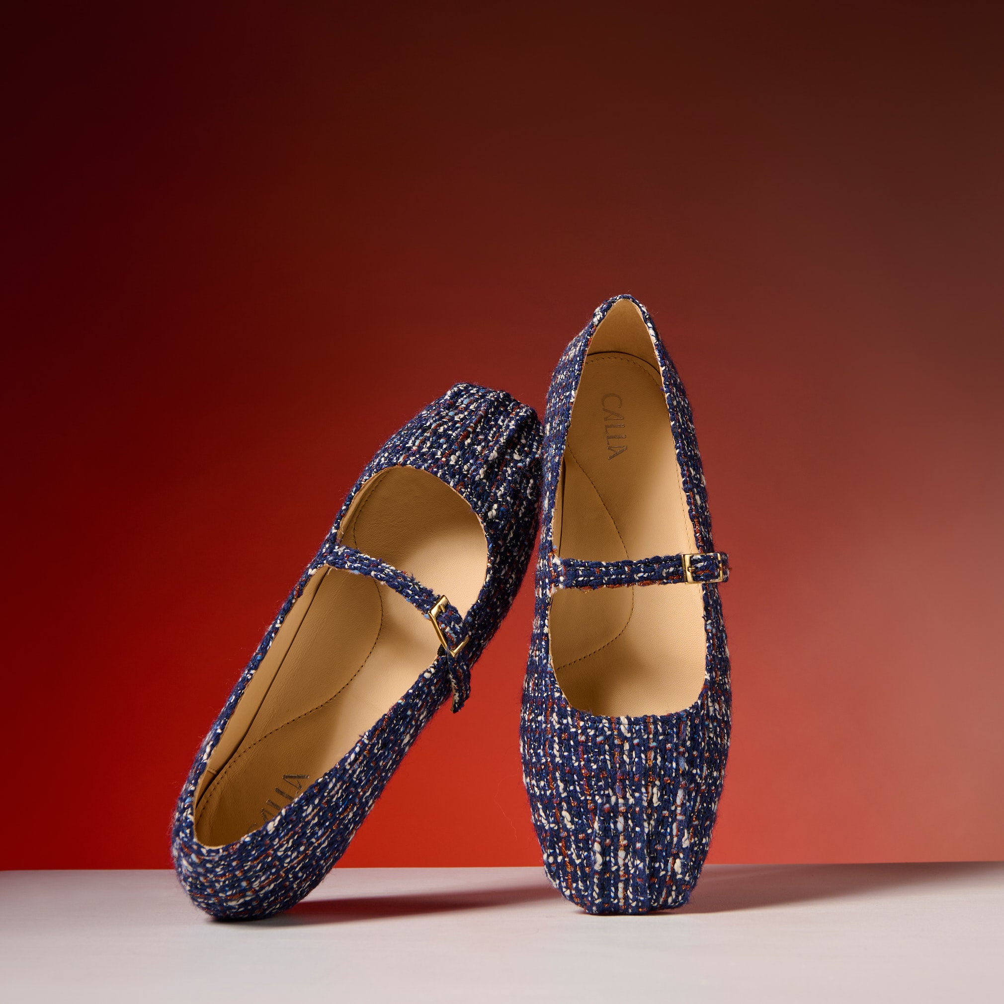 Pair of blue tweed shoes with a strap on a red background