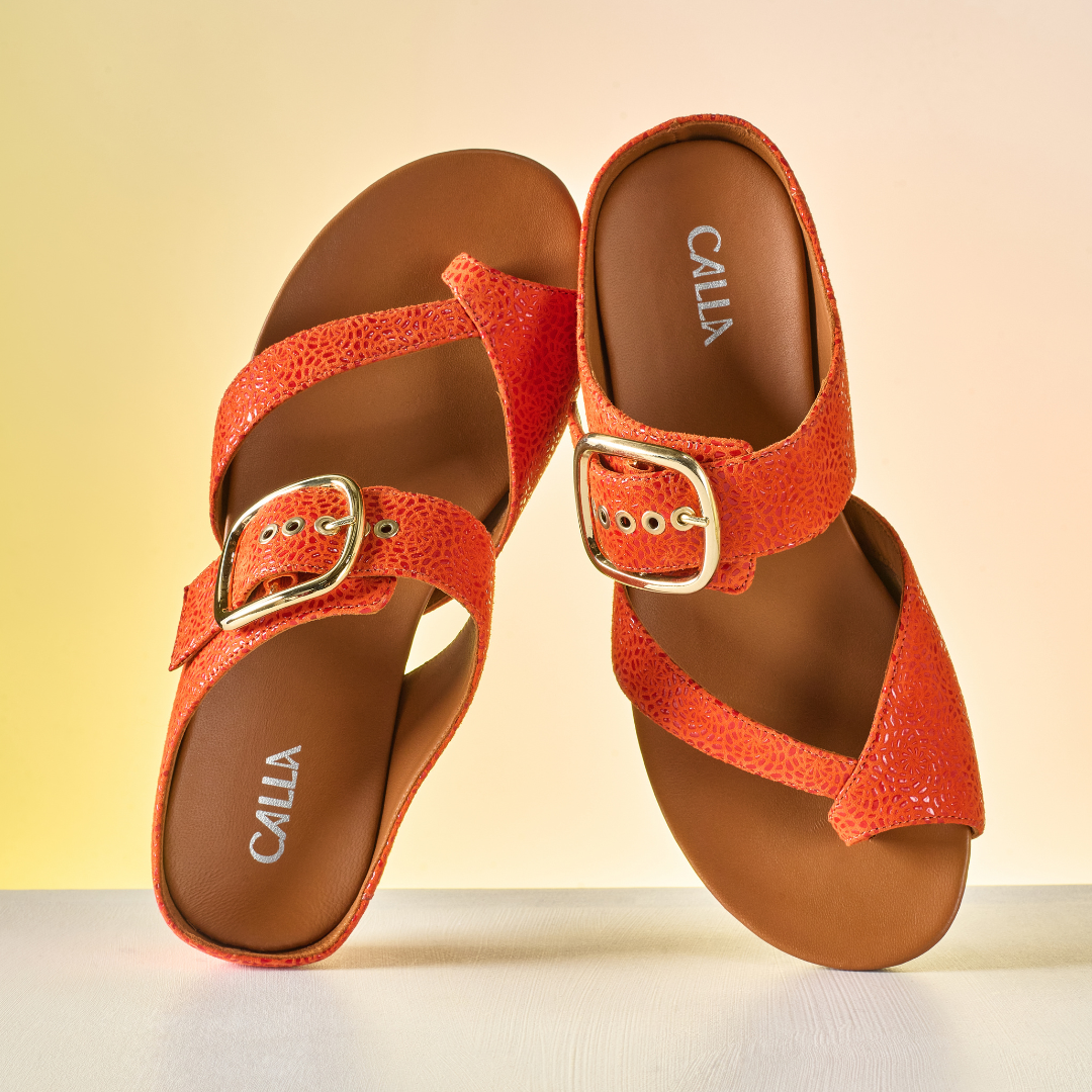 Pair of orange sandals with gold buckles on a light background