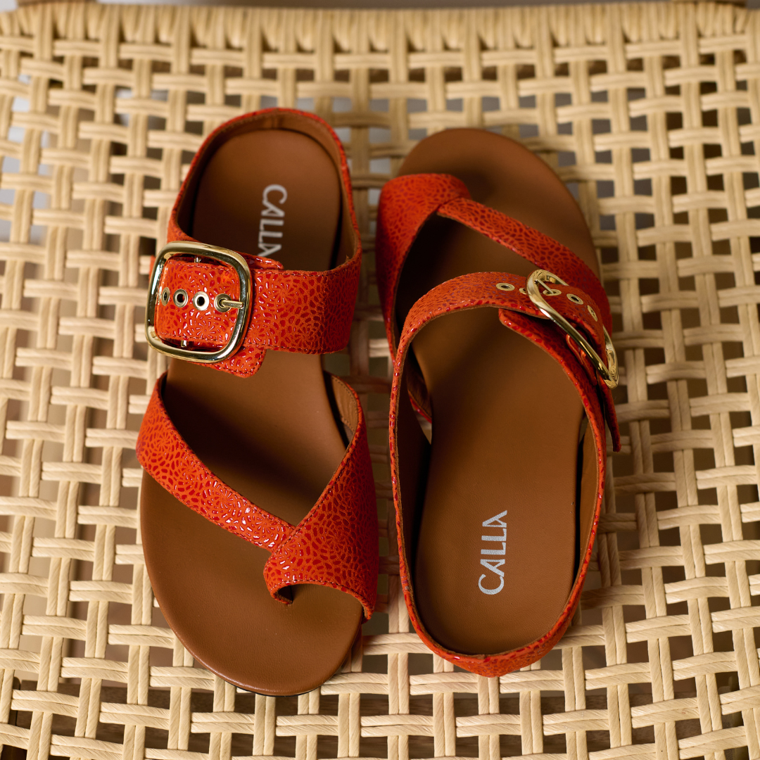 Red sandals with gold buckles on a woven surface