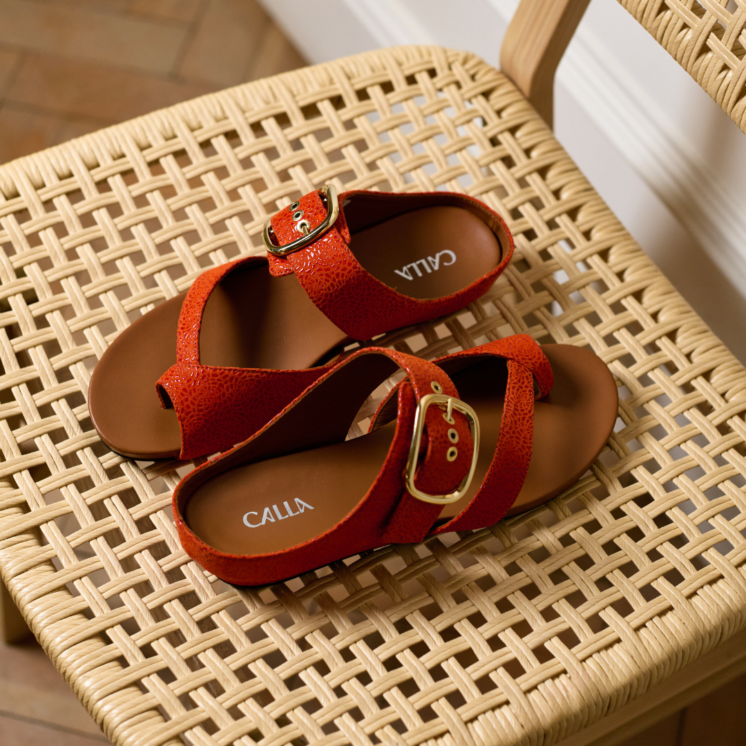 Red sandals with gold buckles on a woven chair