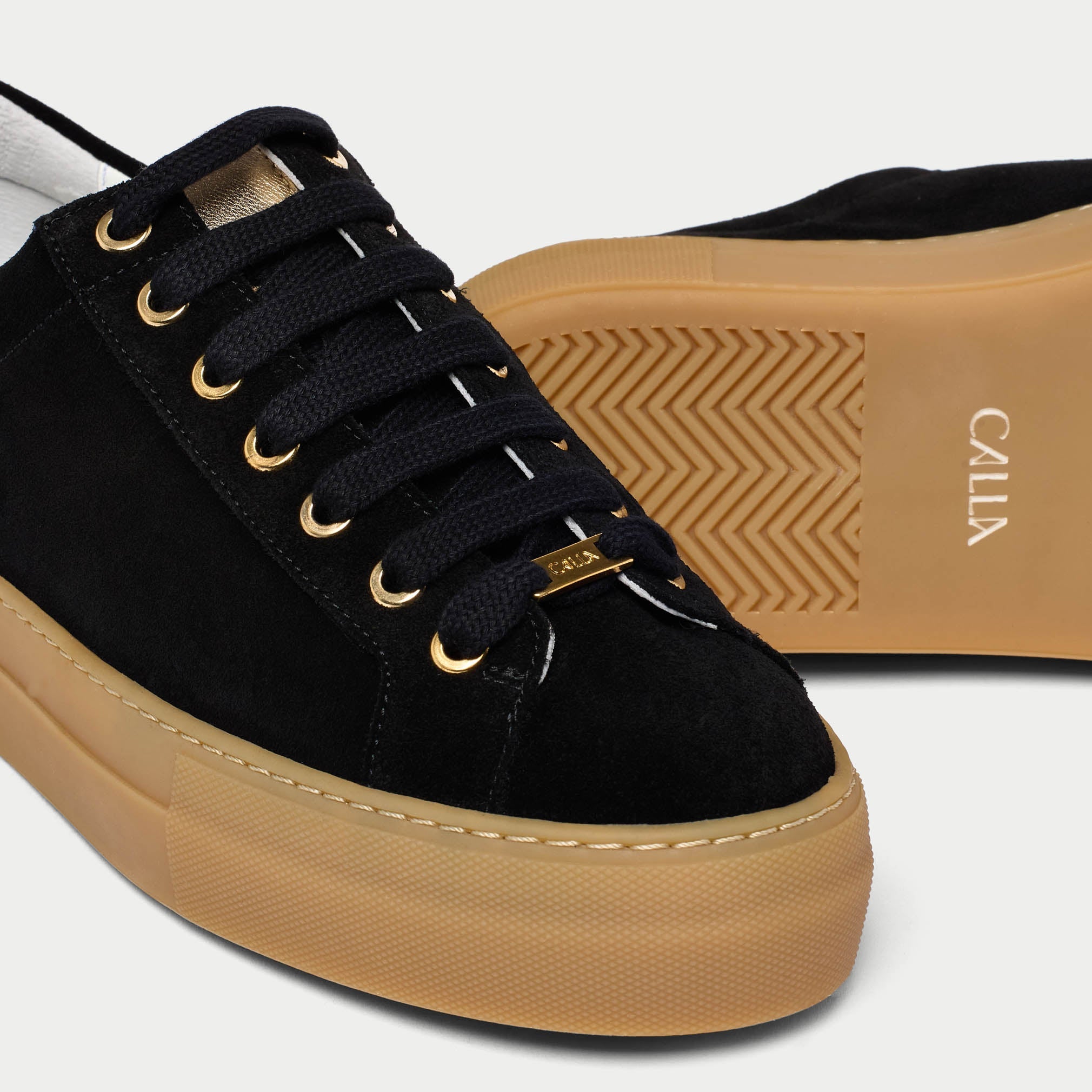 Black Saturn sneakers with tan soles and gold accents on a light gray background tip close-up