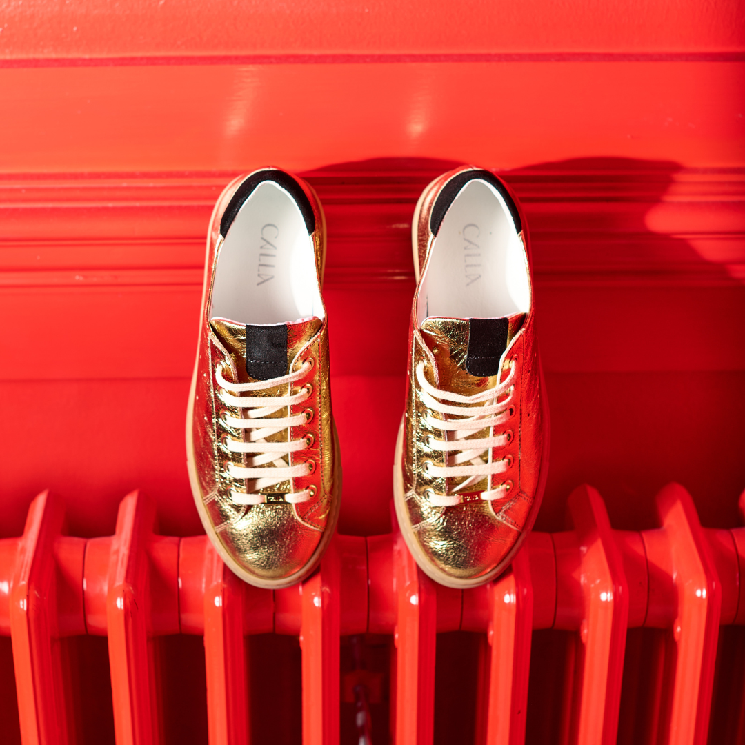 Gold sneakers with white laces on a red surface