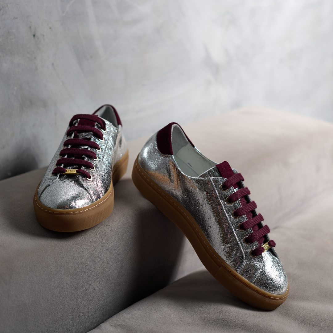 Silver sneakers with maroon laces on a light gray surface