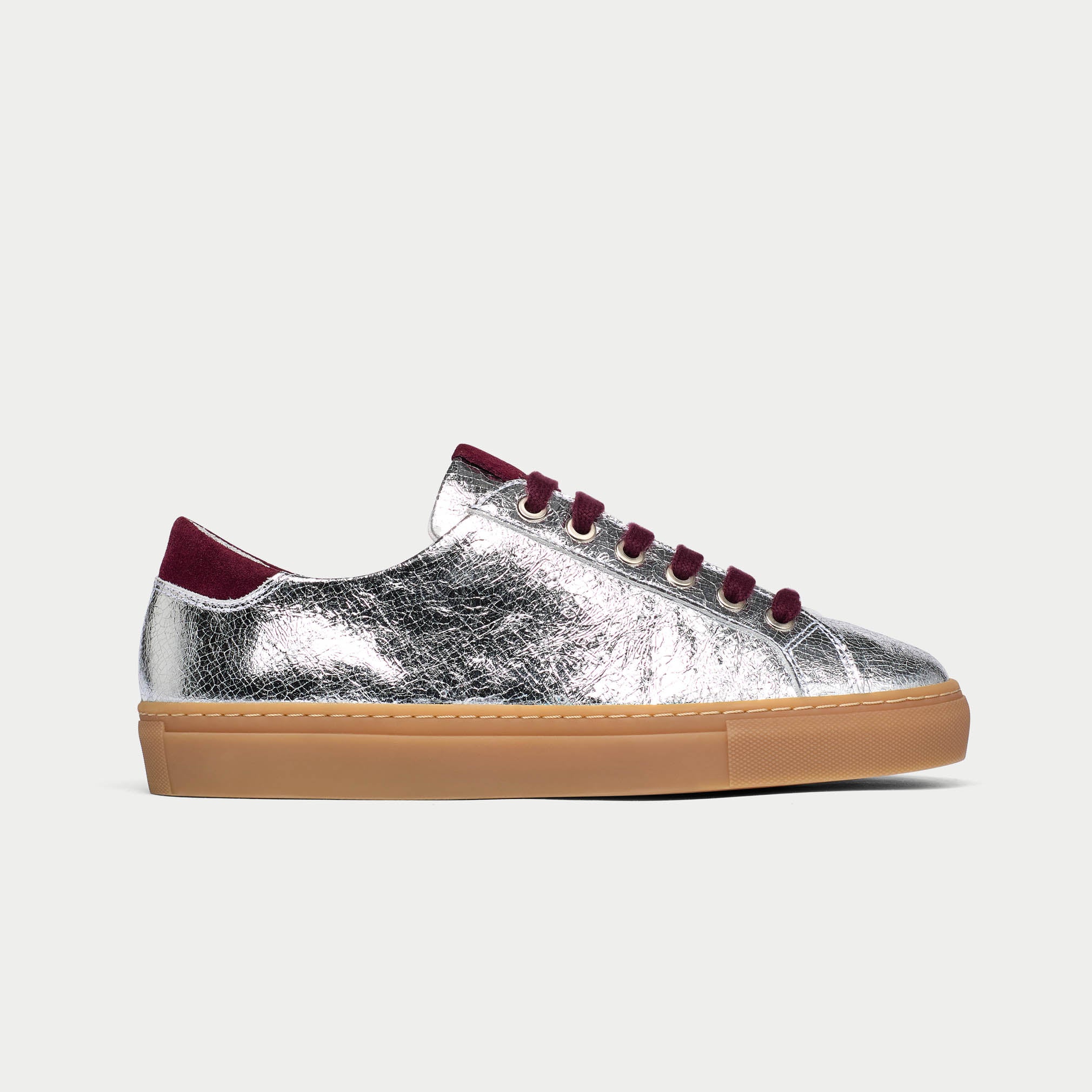Silver star sneaker with burgundy laces and sole on a light gray background side view