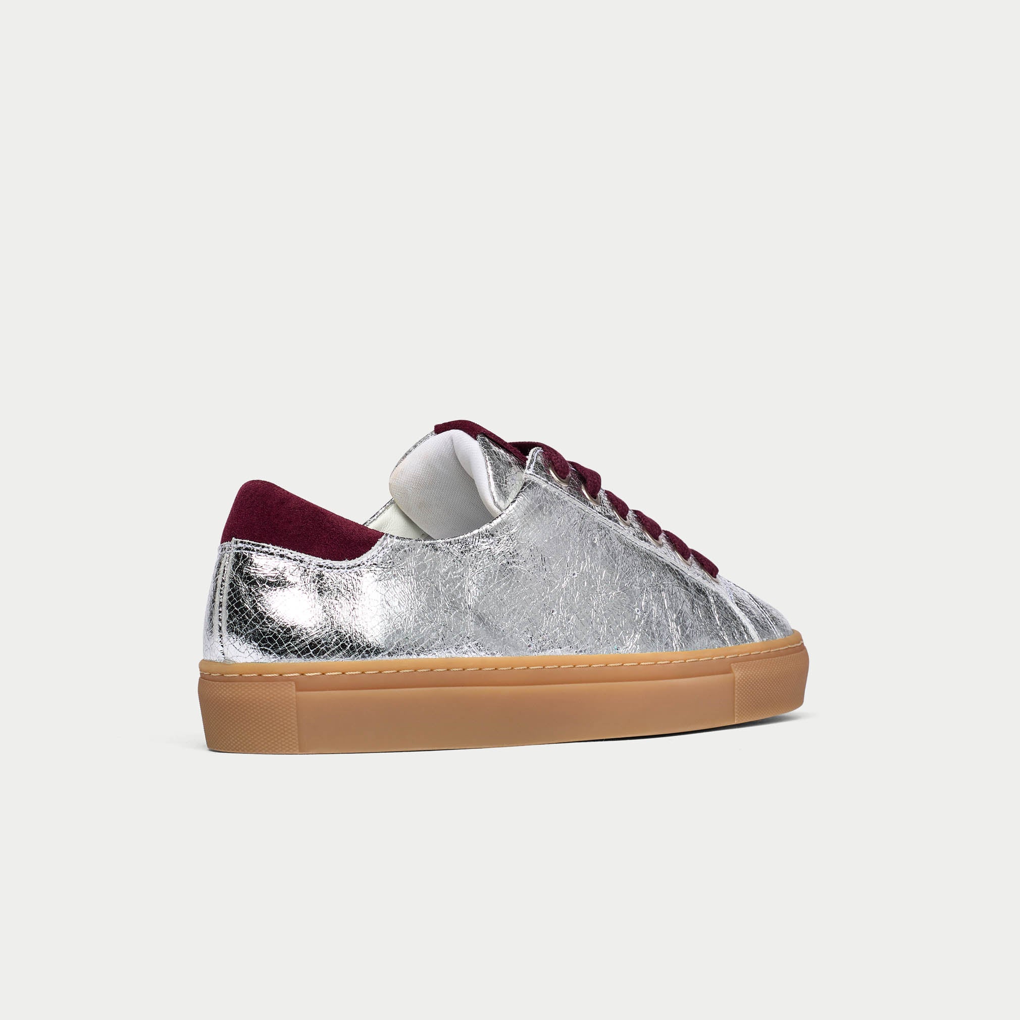 Silver sneaker with red laces and brown sole on a white background