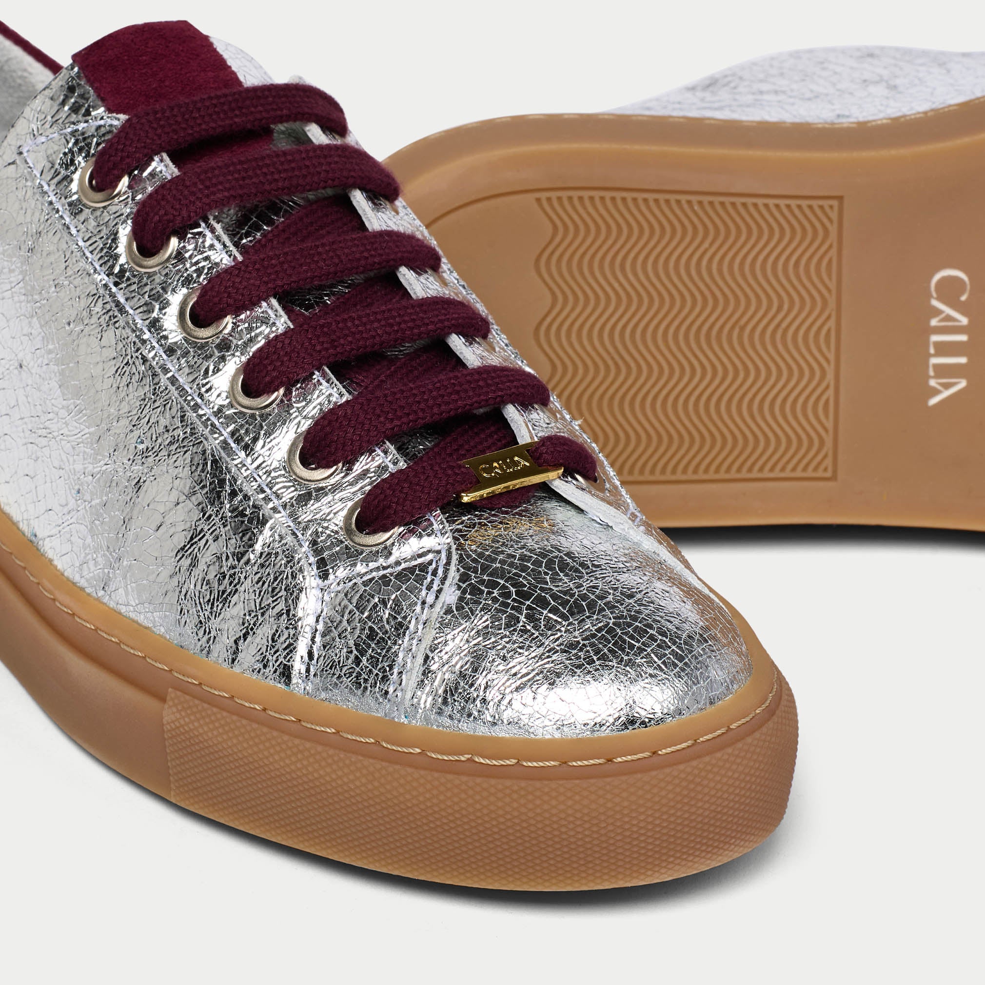 Silver star sneaker with maroon laces and brown sole on a white background