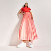 Woman wearing a red top and pink pleated skirt with white star sneakers on a light background