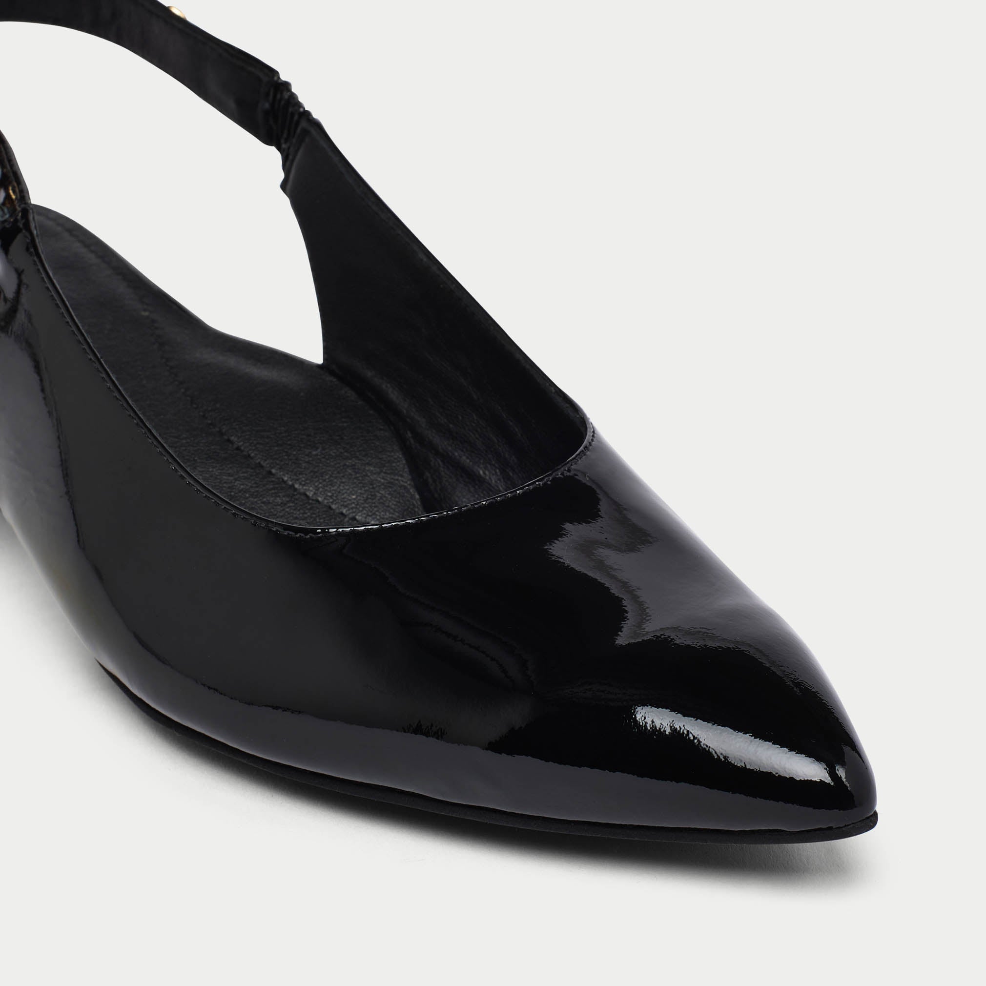 Black patent leather Thea slingback shoe on a light gray background tip close-up