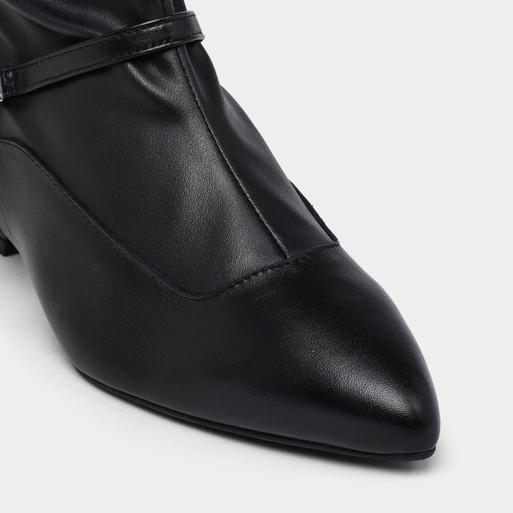 Black leather Veronica shoe with a strap on a light gray background tip close-up