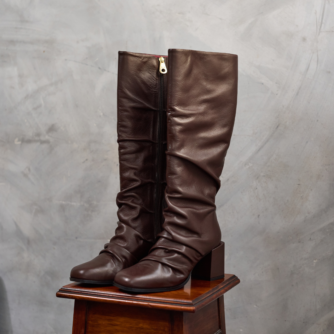 Pair of brown knee-high boots on a wooden block against a gray background
