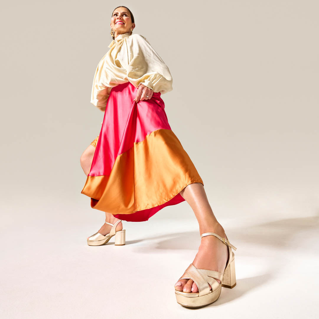 Woman wearing a colorful dress and gracie heels with a plain background