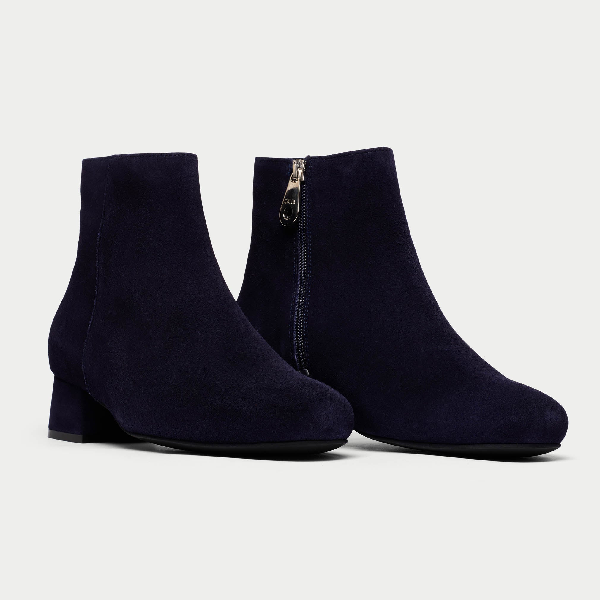 Pair of navy blue ankle boots with a gold zipper on a light gray background