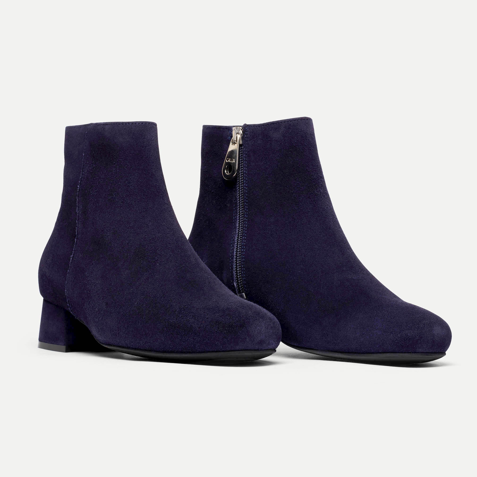 Pair of navy blue ankle boots with a zipper on a light gray background