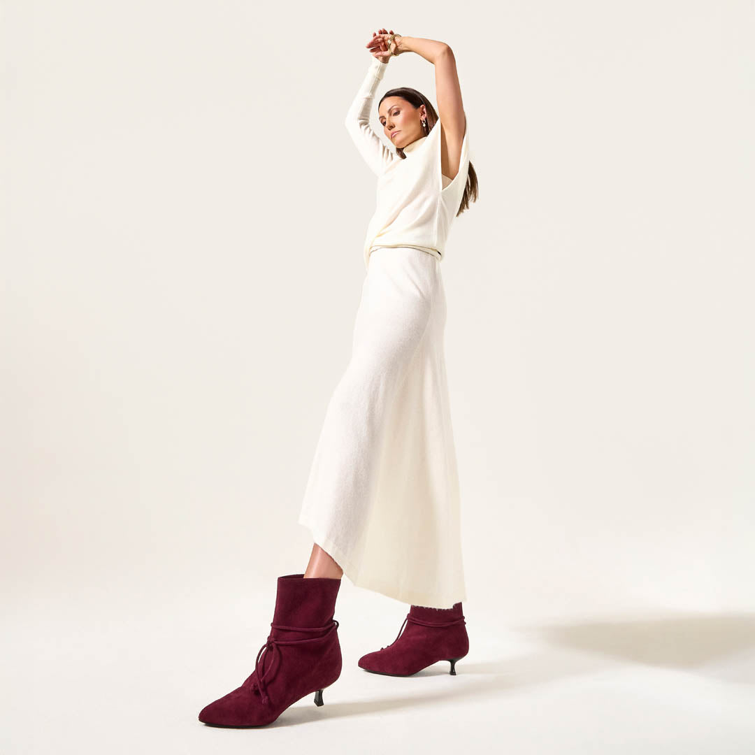 Woman wearing a white outfit with burgundy boots on a light background
