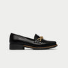 Black loafer shoe with a gold buckle on a light gray background