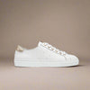 White sneaker with gold accents on a beige background